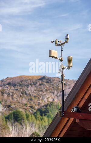 Meteorologische Station auf einem Holzdach platziert. Hinten ein Berg mit Laub und halbwolkenfreiem Himmel Stockfoto