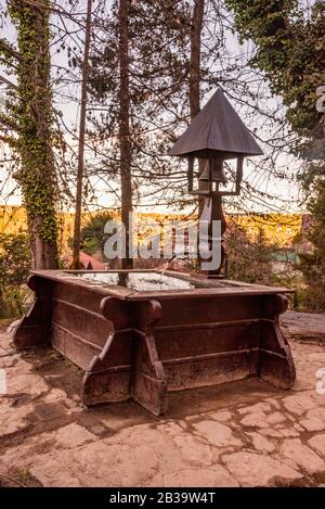 Ein Wasserbrunnen aus Holz mit einem Kirchturm, umgeben von einem kleinen Hain Stockfoto