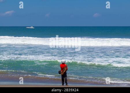 Fischer im Helm sieht aus wie Astronaut steht und angeln Der Strand neben dem Meer Stockfoto