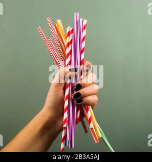 Eine Handvoll plastischer Einweg-Trinkhalme in einer weiblichen Hand auf grünem Hintergrund. Nicht die grünen Dinge, das Umweltverschmutzungskonzept. Stockfoto