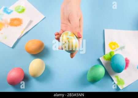 Eine weibliche Hand hält neben anderen bemalten Eiern auf blauem Grund nur ein bemaltes Osterei. Stockfoto