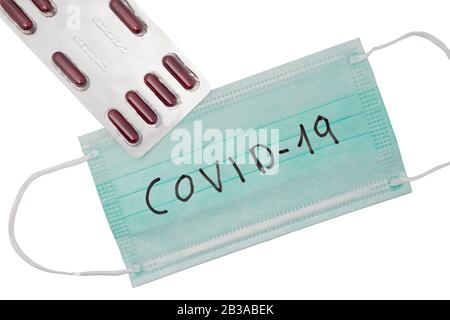 Medizinische Maske auf weißem Hintergrund mit der Aufschrift COVID-19. Und einer Blisterpackung roter Kapseln, Behandlungskonzept. Coronavirus-Epidemie, die bettelt Stockfoto