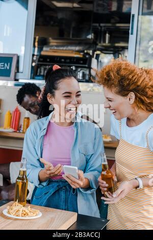 Selektiver Fokus von multikulturellen Mädchen, die in der Nähe von afroamerikanischem Mann und Essenswagen lachen Stockfoto