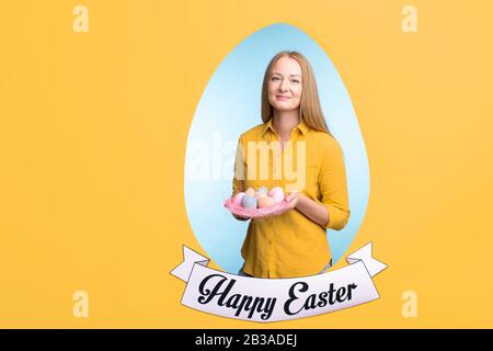 Porträt einer lächelnden jungen blondhaarigen Frau, die mit Ostereiern in eiförmigem Rahmen posiert Stockfoto