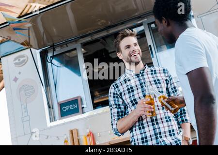 Ein kleiner Blick auf lächelnde multikulturelle Freunde, die Flaschen Bier in der Nähe von Lebensmitteltransportern toben