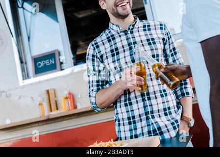 Beschnittenes Bild von fröhlichen multikulturellen Männern, die Bierflaschen toben Stockfoto