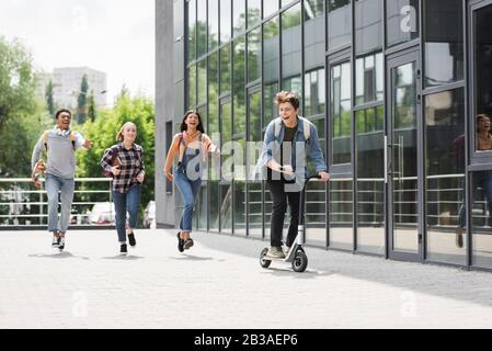 Fröhliche und fröhliche Freunde lächeln, laufen und Motorroller fahren Stockfoto