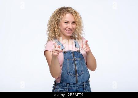 Ja, Sie sind großartig. Schöne junge lächelnde Frau, die auf die Kamera blickt und Sie zeigt, während sie isoliert auf der weißen Studiowand steht. Stockfoto