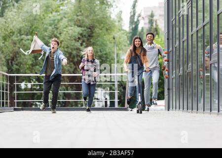 Fröhliche und fröhliche Freunde lächeln, laufen und Motorroller fahren Stockfoto