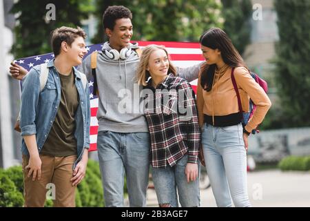 Fröhliche und lächelnde Teenager, die amerikanische Flagge halten und reden Stockfoto