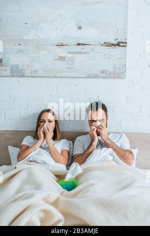 Kranker Ehemann und Frau niesen, während sie im Bett zusammen liegen Stockfoto