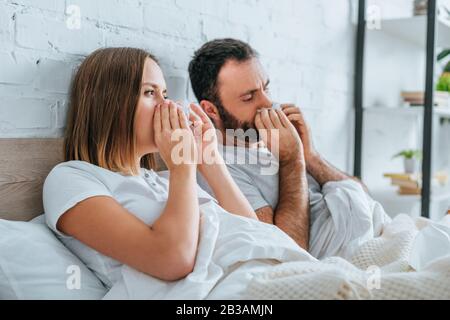 Kranker Ehemann und Frau niesen, während sie im Bett zusammen liegen Stockfoto