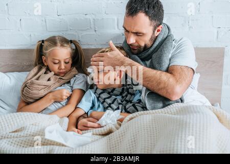 Der besorgte Mann berührt die Stirn des erkrankten Sohnes, während er im Bett zusammen liegt Stockfoto