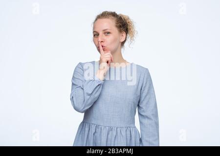 Shush, schweigt, es ist geheim. Die hübsche Frau bittet darum, geheime Informationen vertraulich zu behandeln, gekleidet in blauem Kleid. Studio gedreht Stockfoto