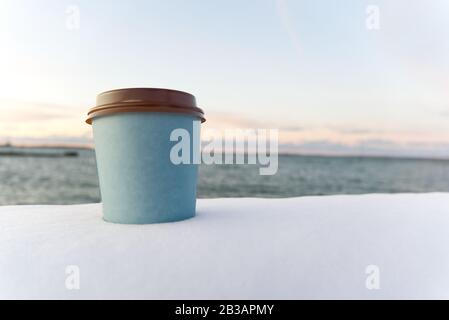 Nehmen Sie Kaffee mit Meeresgrund im Winter. Winterschnee nehmen Sie den Sonnenuntergang über der Kaffeetasse auf dem Meer weg Stockfoto