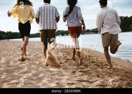 Rückblick auf multiethnische Freunde, die am Strand in der Nähe des Flusses laufen Stockfoto