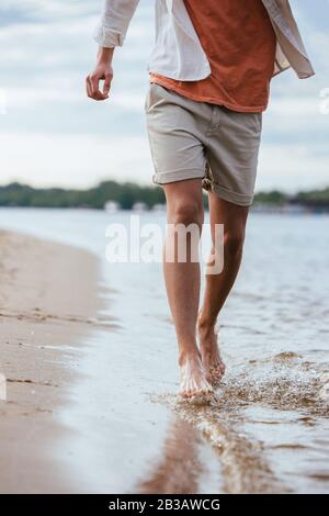 3/4-Blick auf den jungen Mann in Shorts, die am Flussufer laufen Stockfoto