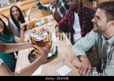 Teilweiser Blick auf die Kellnerin, die in der Nähe von multikulturellen Freunden eine Brille helles Bier hält Stockfoto