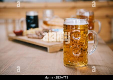 Selektive Konzentration von Becher mit Lagerbier auf Holztisch in der Nähe von Tablett mit Snacks im Pub Stockfoto