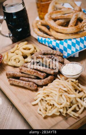 Bratwürste, Zwiebelringe, pommes frites, Brezeln und Tassen mit Bier auf Holztisch im Pub Stockfoto