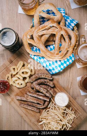 Blick auf Bratwürste, Zwiebelringe, pommes frites, Brezeln und Tassen mit Bier auf Holztisch im Pub Stockfoto