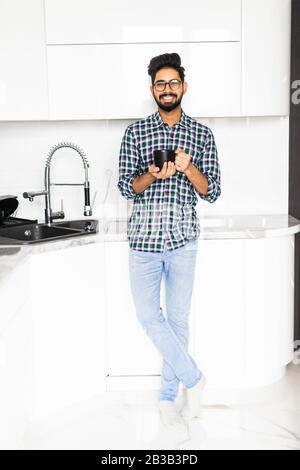 Gutaussehender indianermann in der Küche lächelt und trinkt am Morgen Kaffee. Stockfoto