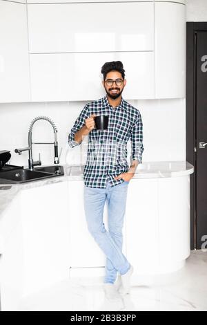 Gutaussehender indianermann in der Küche lächelt und trinkt am Morgen Kaffee. Stockfoto