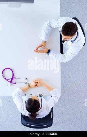 Draufsicht, flacher Lay. Zwei Ärzte in einem Büro im Krankenhaus haben eine Diskussion, während sie mit einem Stethoskop an einem Tisch sitzen Stockfoto