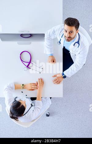 Draufsicht. Zwei Ärzte in einem Büro im Krankenhaus haben eine Diskussion, während sie mit einem Stethoskop an einem Tisch sitzen Stockfoto