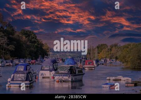 Kleines Pleasure Craft am unteren Rand von Loch Lomond in Balloch, während die Sonne untergeht und einen dramatischen Sonnenuntergang mit strahlender roter Farbe hinterlässt. Stockfoto