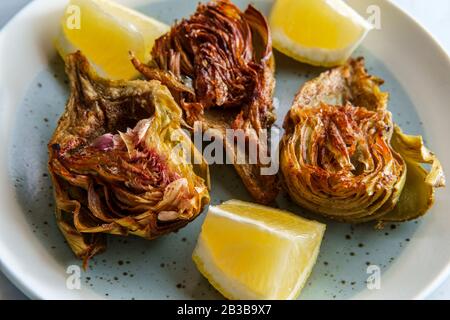 Italienische gebratene halbierte Artischocke mit Zitronenkeilen Stockfoto