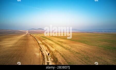 Luftaufnahme von gepflügten landwirtschaftlichen Feldern in Perspektive, Blick auf Ackerflächen im hohen Winkel. Schmutzweg durch die Felder. Kultiviertes Land auf Hügeln von P Stockfoto