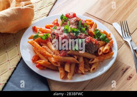 Italienische Penne reißende Pasta mit sugo all'arrabbiata Sauce und Fleischbällchen, garniert mit gehacktem Basilikum und Parmesankäse Stockfoto