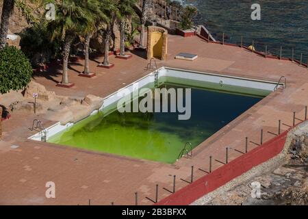 Ein schmutziger und vergangener Pool mit grünem Wasser, einem unvorzüchtigen Pool, einem dreckigen Wasserbecken, einem verlassenen Schwimmbad und einem ruinierten Pool Stockfoto