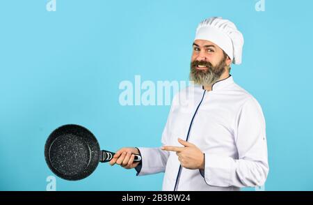 Antihaftbeschichtetes Kochgeschirr. Frittieren ohne Öl. Professionelle küchengeräte. Antihaftpfanne zum Frittieren. Emaillierte Kochgefäße. Mann halte die Pfanne. Frittiermahlzeit. Gesunde Ernährung. Bärtiger Koch bereitet Frühstück zu. Stockfoto