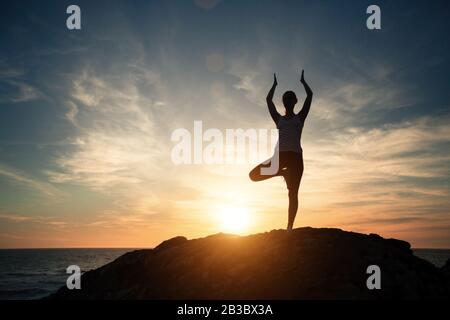 Silhouette der Fitness Yoga-Frau, morgendliche Übungen am Sonnenuntergang am Strand. Stockfoto