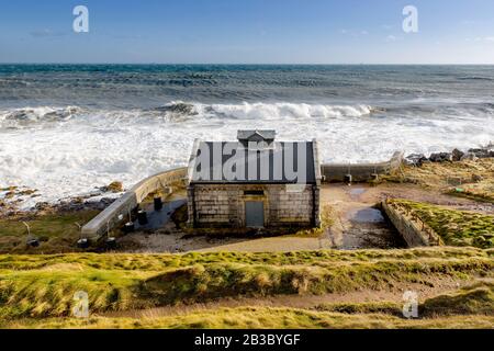 Ein kleines Gebäude am Meer, unterhalb des Aberdeen Lighthouse Girlle Ness und seines Nebelhorns, raue Meereswellen Stockfoto