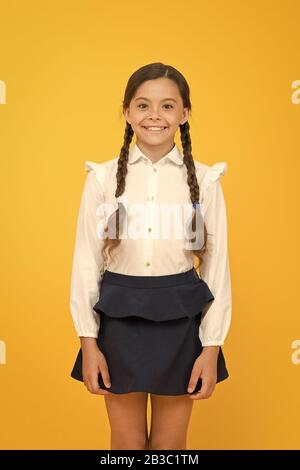 Smart cutie. Süße kleine Mädchen lächelnd auf gelben Hintergrund. Gerne kleine Mädchen tragen Schuluniform. Grundschule Mädchen mit geflochtenem Haar in langen Zöpfen. Adorable girl Stolz, ein Schüler. Stockfoto