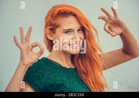 Schöne junge Rotkopffrau Ith langes Ingwerhaar mit Ok-Schild auf Himmelshintergrund. Positive menschliche Emotionen sind Ausdruck Körpersprache Stockfoto