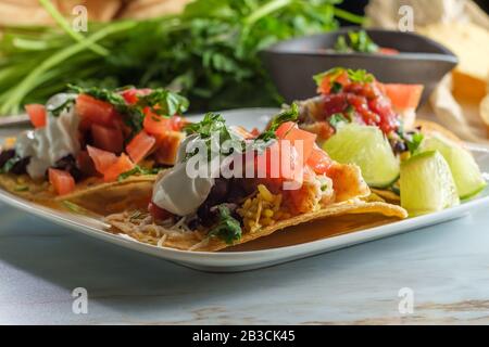 Mexikanisches Huhn tostada flaches Tacos mit Reis, schwarzen Bohnen, Salsa und saurer Sahne Stockfoto