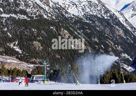 Schneekanonen, die auf der Skipiste Neuschnee bläsen. Skifahrer auf Pisten mit Sesselliften und Pyrenäenbergen im Hintergrund. El Tarter in Grandvalira, Andorra Stockfoto