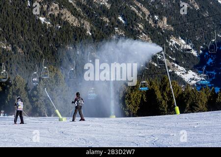 Schneekanonen, die auf der Skipiste Neuschnee bläsen. Skifahrer auf Pisten mit Sesselliften und Pyrenäenbergen im Hintergrund. El Tarter in Grandvalira, Andorra Stockfoto