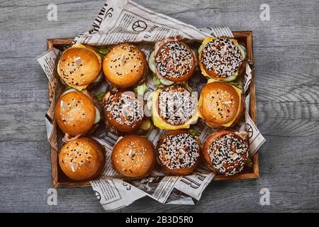 Schmackhafter Käseburger in einer Holzkiste auf hellem Hintergrund. Eine Schachtel mit verschiedenen Burgern, ein Setangebot für ein Unternehmen Stockfoto