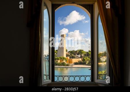 Blick auf Meer, Landschaftsbau und italienisches Segeldenkmal durch ein Bogenfenster an einem sonnigen Tag im Hafen von Brindisi, Italien. Stockfoto