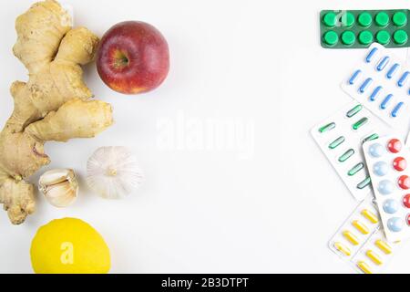 Zitrone, Ingwer, eine Kapelle und Äpfel gegen bunte Tabletten. Das Konzept der Wahl einer gesunden Ernährung im Gegensatz zur Einnahme von Medikamenten Stockfoto
