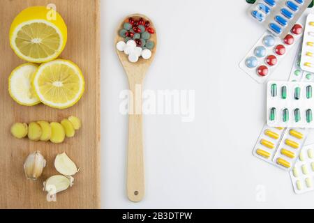 Zitrone, Ingwer und Kapelle gegen mehrfarbige Tabletten. Das Konzept der Wahl einer gesunden Ernährung im Gegensatz zur Einnahme von Medikamenten Stockfoto