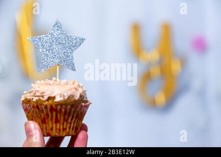 Mädchen Hand hält Preiselbeeren Cupcake mit silberfarbenem Glitzer Sternentopper Stockfoto