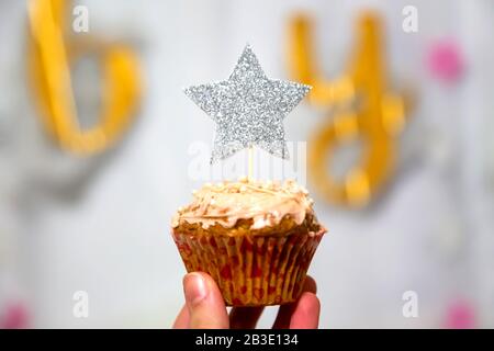 Mädchen Hand hält Preiselbeeren Cupcake mit silberfarbenem Glitzer Sternentopper Stockfoto