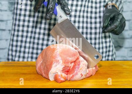 Weibliche Hände in schwarzen Handschuhen schneiden saftige Schweinestücke Stockfoto