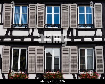 Klassische elsässische Fenster in einem Fachwerkhaus, dekoriert mit Holzschnitzereien und Blumen, Frankreich Stockfoto